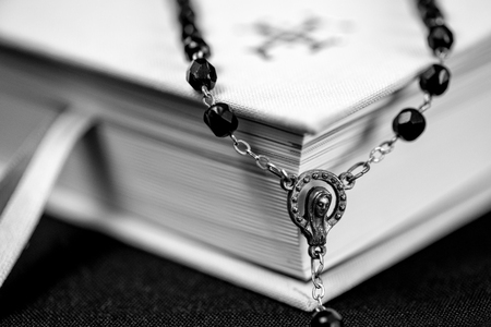 White prayer book and black rosary on the tableの写真素材