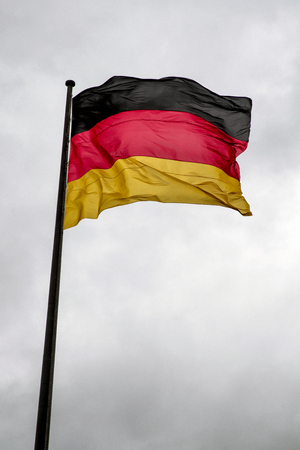 Waving German flag on mast and dark clouds on the skyの写真素材