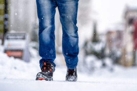 Man walking on snowy sidewalk in winter city. Close up shot on legs and shoes