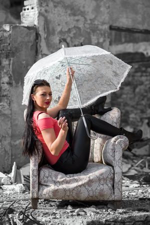 Pretty young model girl with umbrella and cigarette sitting in chairの写真素材