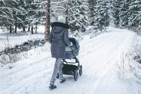 Woman pushing a pram on snowy road in winter nature