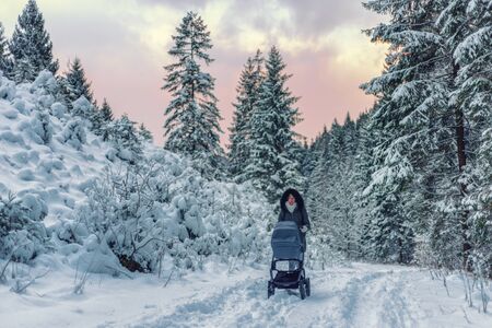 Woman pushing a pram outside in nature in snowy winter forestの写真素材