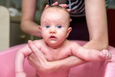 Mother bathing cute baby girl in pink bathtubの写真素材