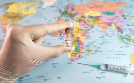 Coronavirus COVID-19 vaccine in hand with protective gloves and injection syringe on map of world at background.の写真素材