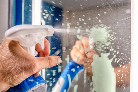 Cleaning bathroom mirror. Spraying detergent in handの写真素材