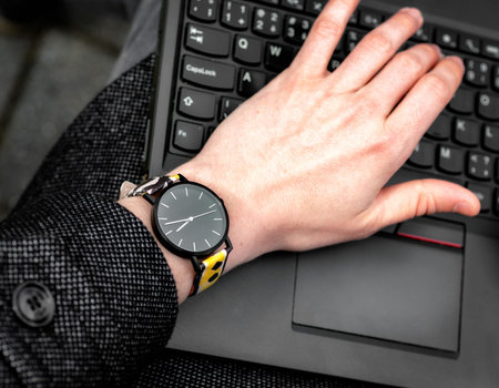 Wristwatch. Hand on the keypad of notebook.