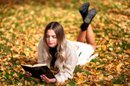Young model girl lying on colorful leaves in autum park and reading a bookの写真素材
