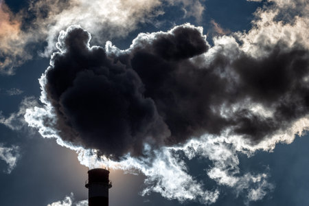 Dark smoke and steam from smokestack  in factory against the sky