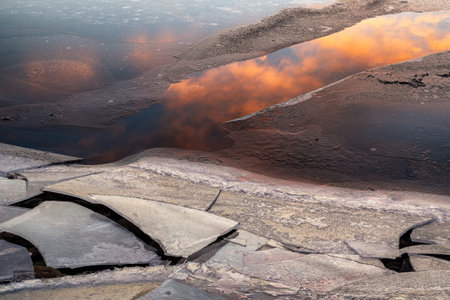 Ice floes on the lake shore. Reflection of colorful clouds on water surface.