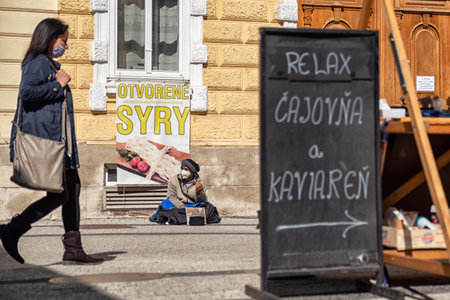 RUZOMBEROK, SLOVAKIA  - MAY 11, 2021: Begging homeless with respirator sitting on ground on roadのeditorial素材