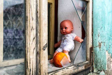 Baby doll in window with broken glass on ruined house.の写真素材