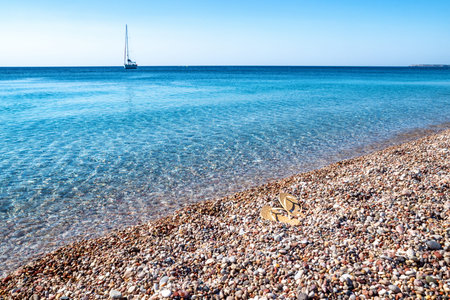 Sandals on the shore with pebble beach. Yacht on the sea at background.の写真素材
