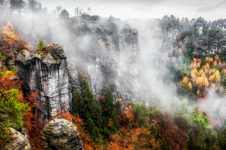 Rock formations and misty weather in colorful autumn forest at Saxon Switzerland national park in Germanyの写真素材