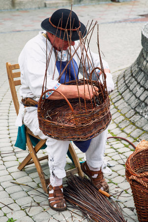 RUZOMBEROK, SLOVAKIA - MAY 13, 2022: Senior craftsman while weaving wicker basketin center of townのeditorial素材