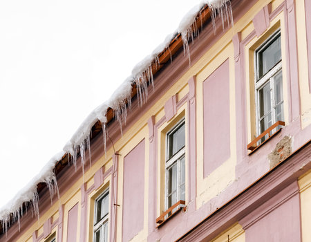 big and Sharp icicles hanging down from roof on facade of building. dangerous Melting ice on...