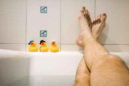Legs of man relaxing in the bath and yellow ducks.