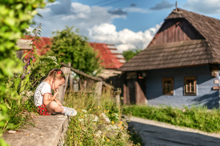 Happy small four years old girl dressed in red folk skirt posing in traditional rural village Vlkolinec with wooden cottages in Slovakiaの写真素材