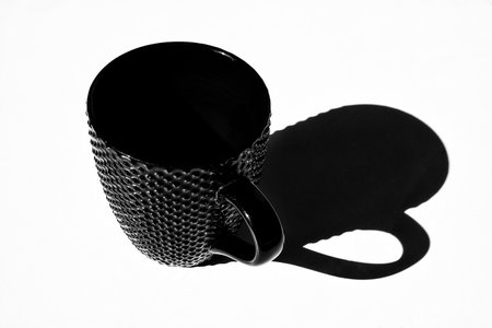 Black cup on white table with dark shadowの写真素材