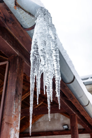 Big icecles hangigng from the roof of the house in cold winter.