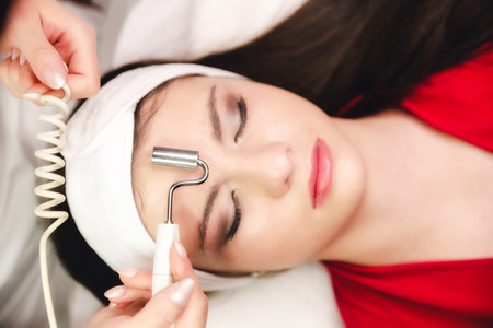 Beautician making facial procedure and anti-aging treatment to a young girl in beauty salon.