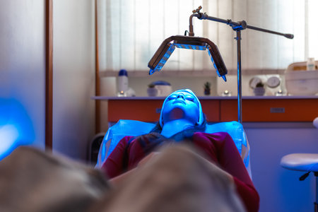 Facial treatment with led therapy. Girl on a light therapy procedure. LED lamp with blue light. Woman in protective glasses..の写真素材