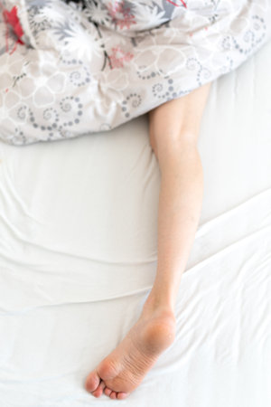 woman s leg sticking out from under the duvet in the bedの写真素材