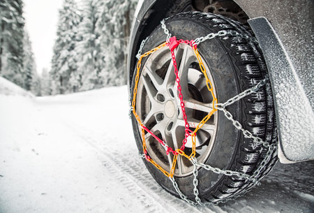 Close-up of a car tire with snow chains on a snowy forest road, providing safe winter driving on icy...