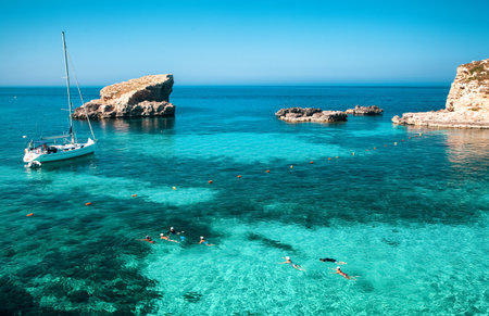 Blue Lagoon with turquoise sea water, yacht and people swimming near rocky coast of Comino island, popular summer travel destination in Malta.の写真素材