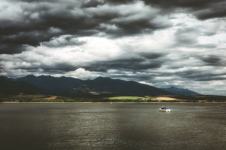 Liptovska Mara reservoir with tourist boat sailing under dramatic cloudy sky, Western Tatras mountains in background, scenic summer landscape in Slovakia region Liptov.の写真素材