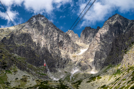 Tatranska Lomnica, Slovakia â June 21, 2025: Red cabin of the cable car ascending to Lomnicky peak in the High Tatras mountains under blue sky with rocky ridges and alpine landscape.の写真素材