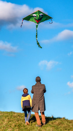 Smiling father teaching son to fly kite together under bright blue sky, symbol of family love, guidance and playful outdoor experienceの写真素材