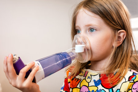 Little girl using inhaler with mask during home respiratory therapy. Image symbolizing pediatric asthma prevention, medication and daily healthcare routine.の写真素材