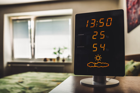 Modern digital weather station with illuminated display showing indoor temperature and humidity in...
