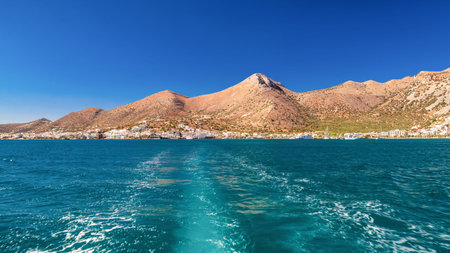 Beautiful panoramic view of Elounda on Crete, Greece, captured from a boat over turquoise sea. Scenic summer landscape with mountains, blue sky and coastal town.の写真素材