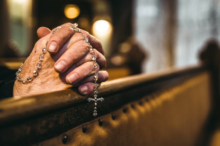 Close up of elderly hands holding rosary in church bench with warm light and soft background. Spiritual moment symbolizing faith and religion.の写真素材