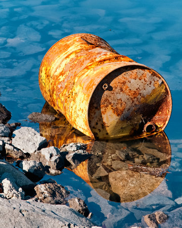 Rusty yellow oil barrel lying in polluted lake, symbol of water contamination and environmental damage.の写真素材