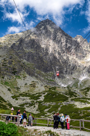 Tatranska Lomnica, Slovakia - June 21 2025: Group of tourists standing at viewpoint and watching red cable car to Lomnicky peak in High Tatras mountains during sunny summer day.の写真素材