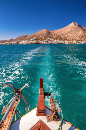 Boat sailing on turquoise sea near Elounda on the island of Crete, with clear blue sky, mountains and coastal town visible in the background.の写真素材