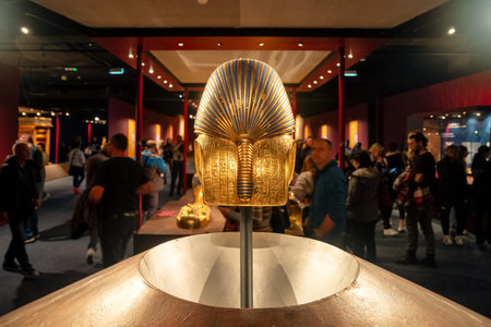 Bratislava, Slovakia - November 15, 2025: Visitors viewing a golden funerary mask during a Tutankhamun exhibition, surrounded by Egyptian artifacts in the museum hall.のeditorial素材