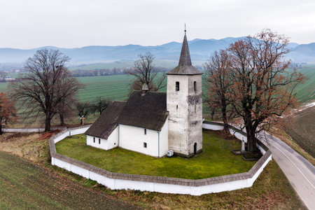 Drone close view of the historic church tower and defensive wall in Ludrova, Slovakia, set in the rural Liptov landscape with autumn colors, ideal for themes of heritage, architecture and travel.の写真素材