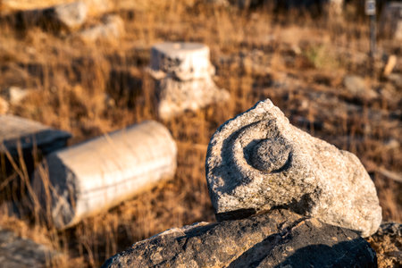 Weathered marble column fragment from an ancient archaeological site near Panormos, Crete, photographed in warm evening light. The close-up highlights the texture and craftsmanship of the ancient stone with the surrounding ruins softly blurred in the background.の写真素材