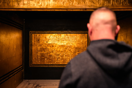 Visitor observes a golden shrine panel from Tutankhamunâs burial chamber at an exhibition, with warm light highlighting ancient pharaoh symbols and Egyptian cultural details.の写真素材