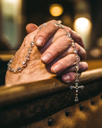 Closeup of hands holding a rosary during prayer inside a church with warm spiritual light and intimate atmosphere.の写真素材