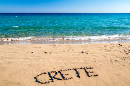 Create word arranged from stones on sandy beach by clear turquoise sea near Xerokambos on eastern Crete, Greece. Summer travel and minimal concept.の写真素材