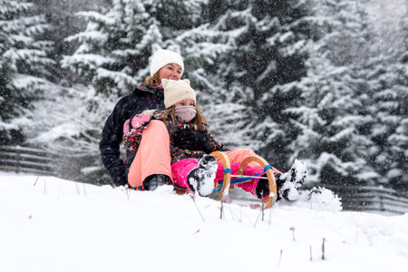 Mother and child sledding fast downhill through fresh snow. Dynamic winter action, outdoor fun,...