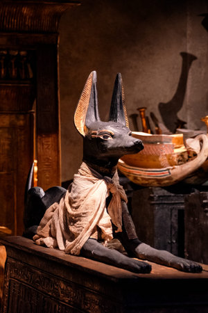 Bratislava, Slovakia - November 15, 2025: Detailed view of an Anubis statue surrounded by Egyptian replicas at the Tutankhamun exhibition in a warmly lit museum environment.のeditorial素材