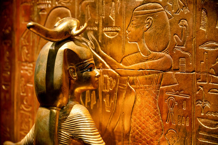 Golden statue of Pharaoh Tutankhamun positioned in front of ancient Egyptian reliefs. The scene...