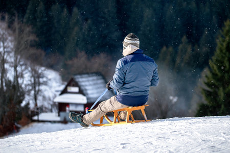 Rear view of a person resting on a wooden sled on a snowy slope during winter, enjoying outdoor leisure activity in cold mountain conditions.の写真素材