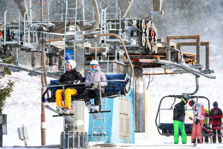 Ruzomberok, Slovakia - December 30, 2025: Children riding a chairlift in falling snow at mountain ski resort, capturing family winter recreation, ski holidays and seasonal tourism in alpine environment.の写真素材