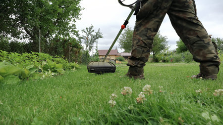 The gardener mows the grass in the garden with a brushcutter